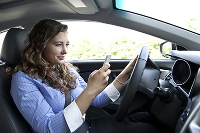 Young woman looking at phone while driving | Smartphones: Increasing Accidents and Raising Rates
