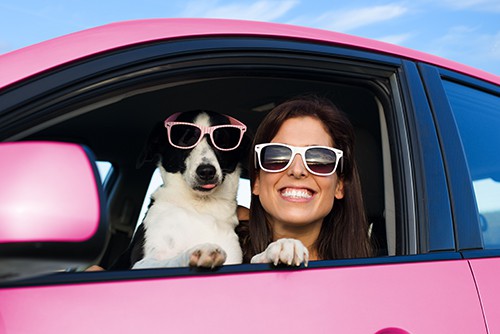 Woman and dog in pink car on summer road trip wearing sunglasses | Interesting Car Color Facts You Might Find Surprising