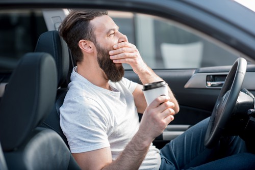 yawning man with a beard holding coffee and Driving While Drowsy 