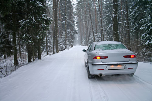 white car driving down snowy forest road | Winter Driving Essentials 